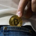 Close-up of hand putting Bitcoin in jeans pocket symbolizing cryptocurrency savings.